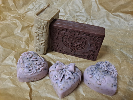 Presentación de tres tipos de jabones 100% veganos y artesanos: de té con forma de corazón, de café con forma de libro y de cacao con forma de cajita